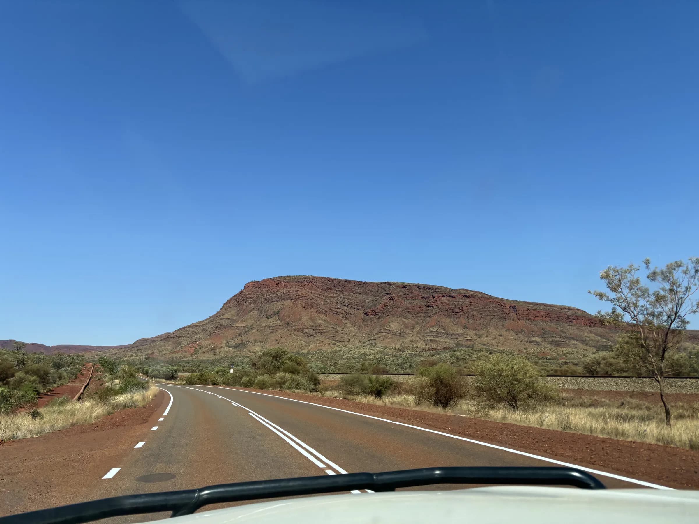 Pilbara highway running towards a red mesa under a blue sky