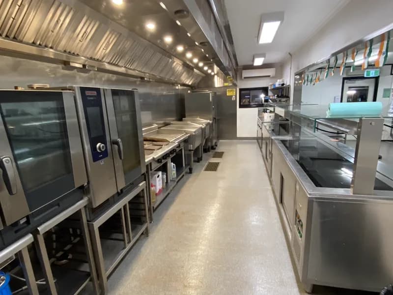 Mine-camp kitchen cook line with combi ovens and griddles under a long exhaust canopy, floor clean and dry