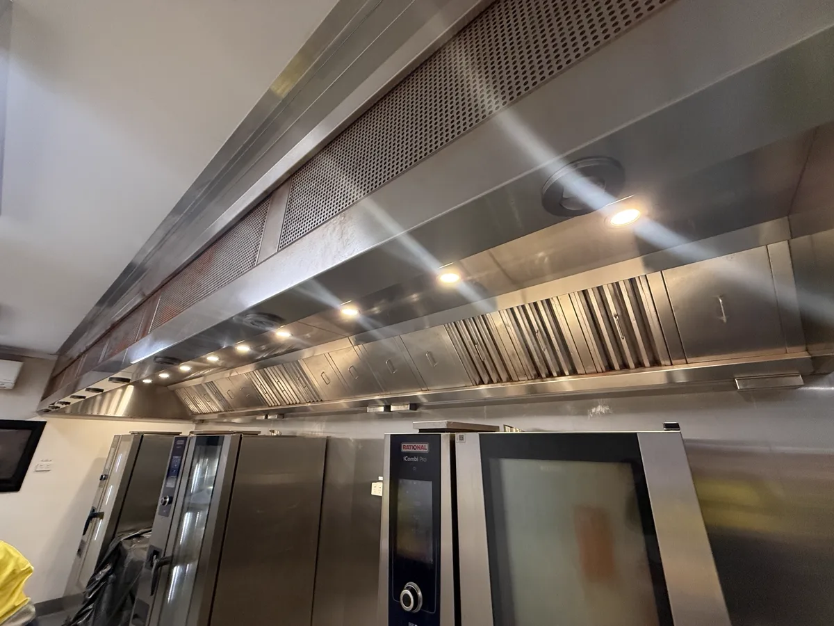 Cleaned commercial kitchen exhaust canopy running above the cook line, filters and lights back in place